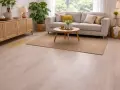 Un salon moderne avec un canapé gris, une table basse en bois et un tapis. Une tache jaune sur le lino, près d'un buffet en rotin, semble tenace.