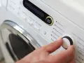 Main d'une personne réglant la température de lavage d'une couette sur un panneau de commande de machine à laver.