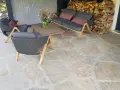 Terrasse en pierre naturelle extérieure, protégée par un imperméabilisant, avec mobilier de jardin confortable et un bouquet de fleurs sauvages.