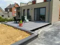 Une terrasse moderne avec un dallage gris sur plots, prête pour un couler dalle. Mobilier de jardin et végétation environnante.