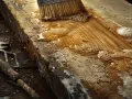 Un pinceau applique un mélange d'huile de lin et d'essence de térébenthine sur une planche de bois brute, près d'une vieille pierre.
