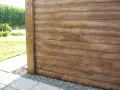 Bardage en bois de mélèze, traité pour l'extérieur, avec un poteau vertical. Le bois présente des nœuds et un grain prononcé.