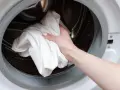Main tenant met une serviette blanche dans le tambour d'une machine à laver pour dissoudre lessive durcie.