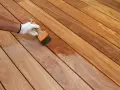 Application d'un produit protecteur sur un platelage en bois exotique, révélant sa beauté naturelle.