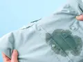 Main d'une personne tenant une chemise bleu pâle avec une grande tache d'huile sur le devant, prête à enlever une tache d'huile avec du bicarbonate.