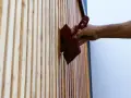 Maintenir son bois en parfait état : une main applique une huile protectrice sur des lattes de bois, comme pour fabriquer son huile de teck.
