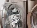 Machine à laver avec une porte ouverte, remplie de linge gris. Choisir la lessive la moins toxique pour un lavage sain.
