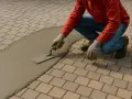 Un ouvrier utilise une truelle pour lisser du mortier sur des pavés autobloquants, préparant le terrain pour une nouvelle finition.