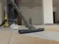 Un aspirateur en action pour enlever l'enduit sur le carrelage. La poussière est aspirée, laissant le sol propre.
