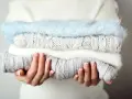 Pile de pulls en laine douce, gris et blanc, avec un pull bleu ciel. Idéal pour savoir comment detacher un pull blanc et le garder comme neuf.