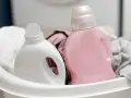 Deux bouteilles de lessive, une blanche et une rose, dans un panier avec du linge.