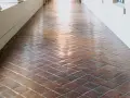 Un couloir avec un carrelage en terre cuite, dont la surface semble avoir été traitée pour vitrifier un carrelage, reflète la lumière.