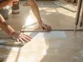 Pose d'un carrelage imitation travertin. Mains ajustant une dalle sur le lit de mortier. Outil de carreleur à proximité.