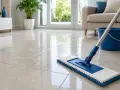 Un balai bleu et blanc est prêt à laver le carrelage sans trace. Un seau bleu est à proximité.