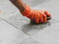 Main tenant, ganté, frotte le sol carrelé avec une brosse pour nettoyer le ciment sec.
