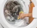 Main d'une personne utilisant un chiffon jaune pour nettoyer l'intérieur d'une machine à laver, une méthode naturelle pour nettoyer machine a laver vinaigre.