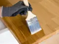 Main tenant avec un pinceau pour enlever l'huile de lin sur du bois.