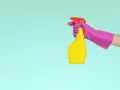 Main tenant, une main gantée de rose tient un flacon jaune prêt à nettoyer le sol en vinyle avec du vinaigre blanc.