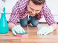 Un homme, muni de gants et d'une éponge, s'agenouille pour nettoyer une tache sur le parquet.