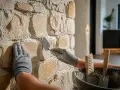 Application de mortier pour comment restaurer la pierre de tuffeau. Une main gantée tient une truelle, l'autre maintient la pierre.