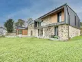 Une maison en pierre rénovée, mêlant tradition et modernité avec des touches de bois et de métal. Un jardin verdoyant entoure cette demeure.