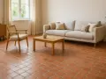 Un salon cosy avec un canapé clair, un fauteuil en rotin et un sol en **sol tomette ancienne** réchauffant l'atmosphère.