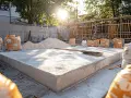 Préparation pour rénover une terrasse en dalle béton : sacs de ciment, sable et une dalle fraîchement coulée sous le soleil.