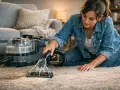 Femme à genoux, utilisant un appareil pour shampouiner tapis. La machine projette de l'eau et aspire la saleté pour un nettoyage en profondeur.