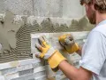 Pose de pierre de parement en quinconce. Un artisan pose des pierres naturelles sur un mur avec du mortier.