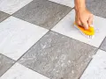 Main tenant utilise une brosse jaune pour faire briller le carrelage, révélant sa beauté naturelle.