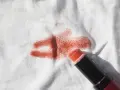 Un bâton de rouge à lèvres orange est posé sur un tissu blanc, laissant une tache rouge à lèvre.