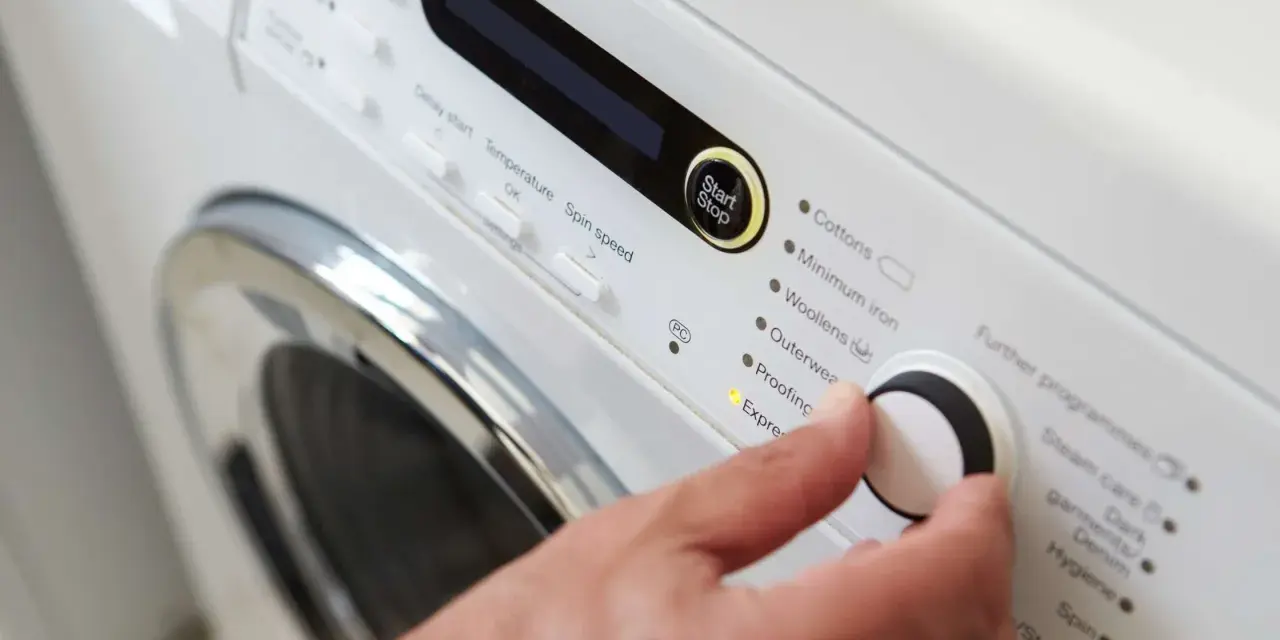 Main d'une personne réglant la température de lavage d'une couette sur un panneau de commande de machine à laver.