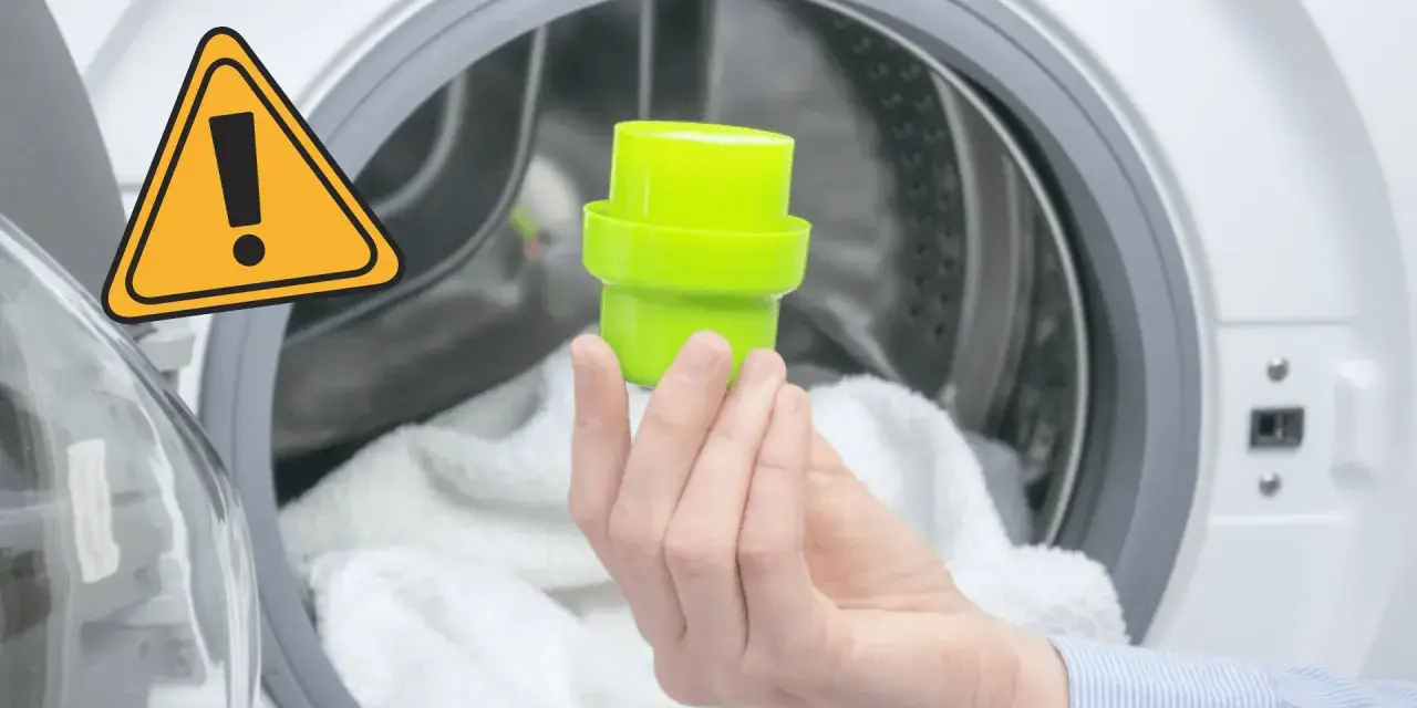 Main dans la machine à laver, tenant un bouchon vert pour le bac adoucissant. Un panneau d'avertissement jaune est visible.