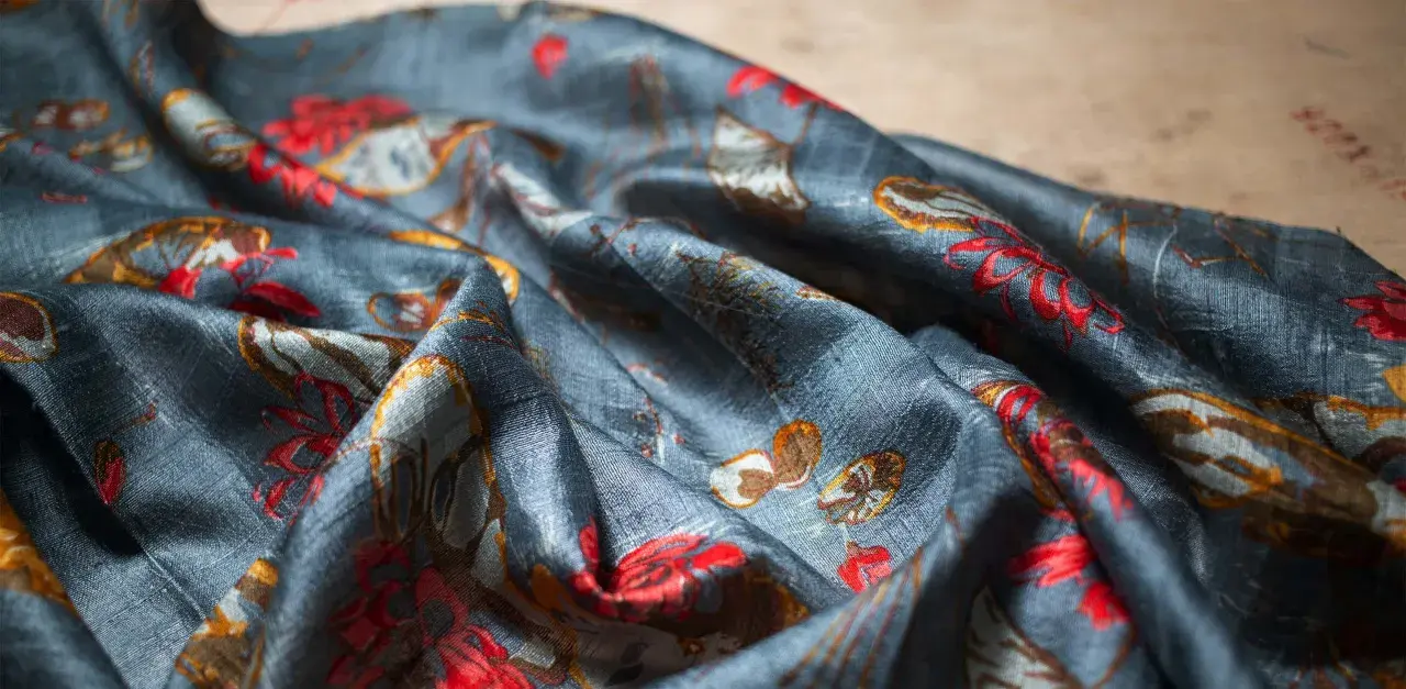 Tissu de soie bleu nuit avec un motif de fleurs rouges et de feuilles dorées. Une tache de gras sur soie, subtile, se fond dans le motif.