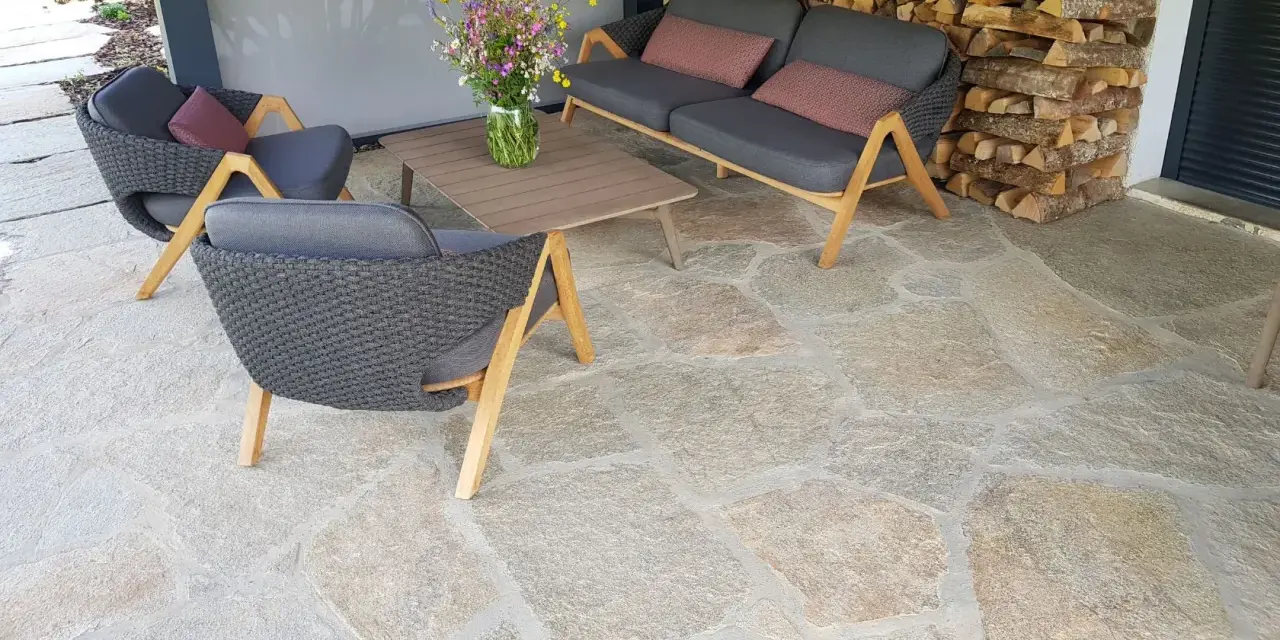 Terrasse en pierre naturelle extérieure, protégée par un imperméabilisant, avec mobilier de jardin confortable et un bouquet de fleurs sauvages.