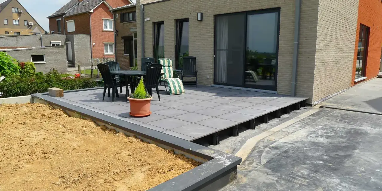 Une terrasse moderne avec un dallage gris sur plots, prête pour un couler dalle. Mobilier de jardin et végétation environnante.