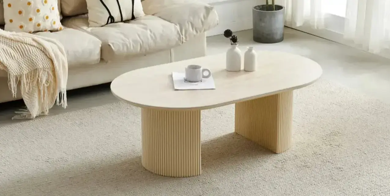 Table basse ovale avec pieds cannelés, sur un tapis doux. Quelle déco avec du travertin, une tasse et des vases sur la table.