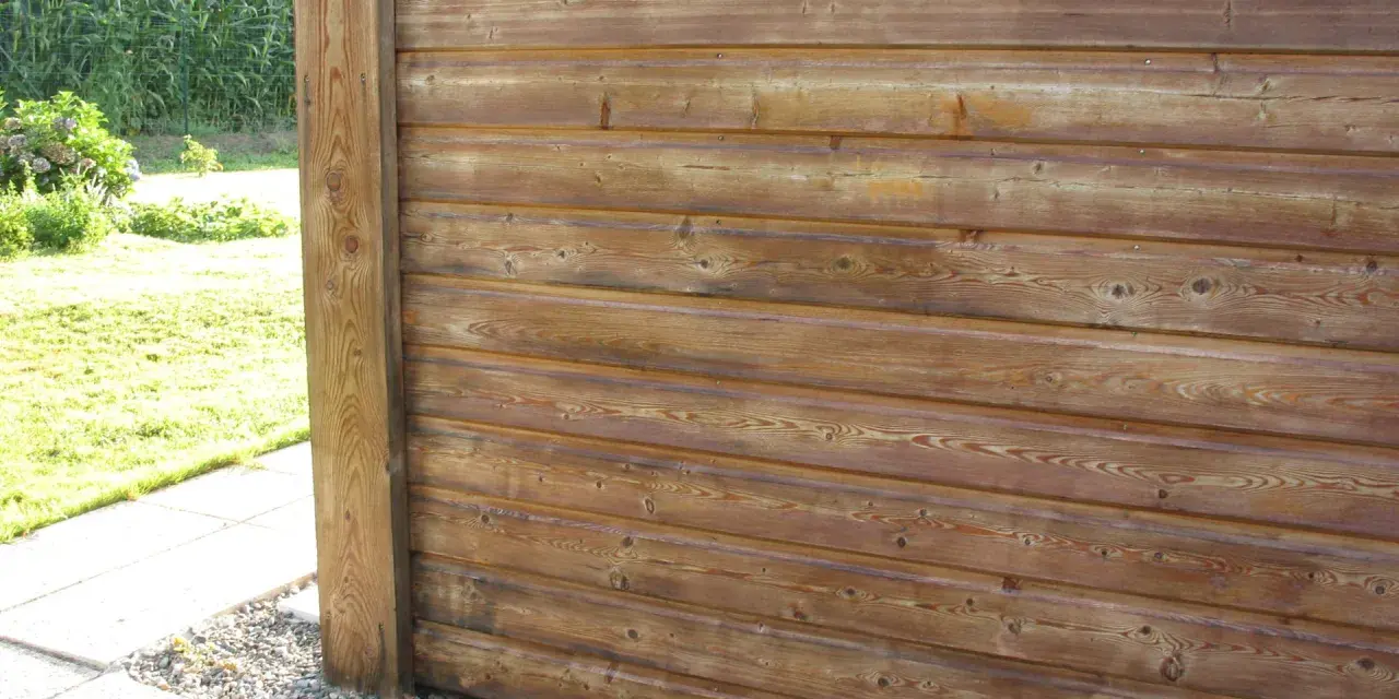 Bardage en bois de mélèze, traité pour l'extérieur, avec un poteau vertical. Le bois présente des nœuds et un grain prononcé.