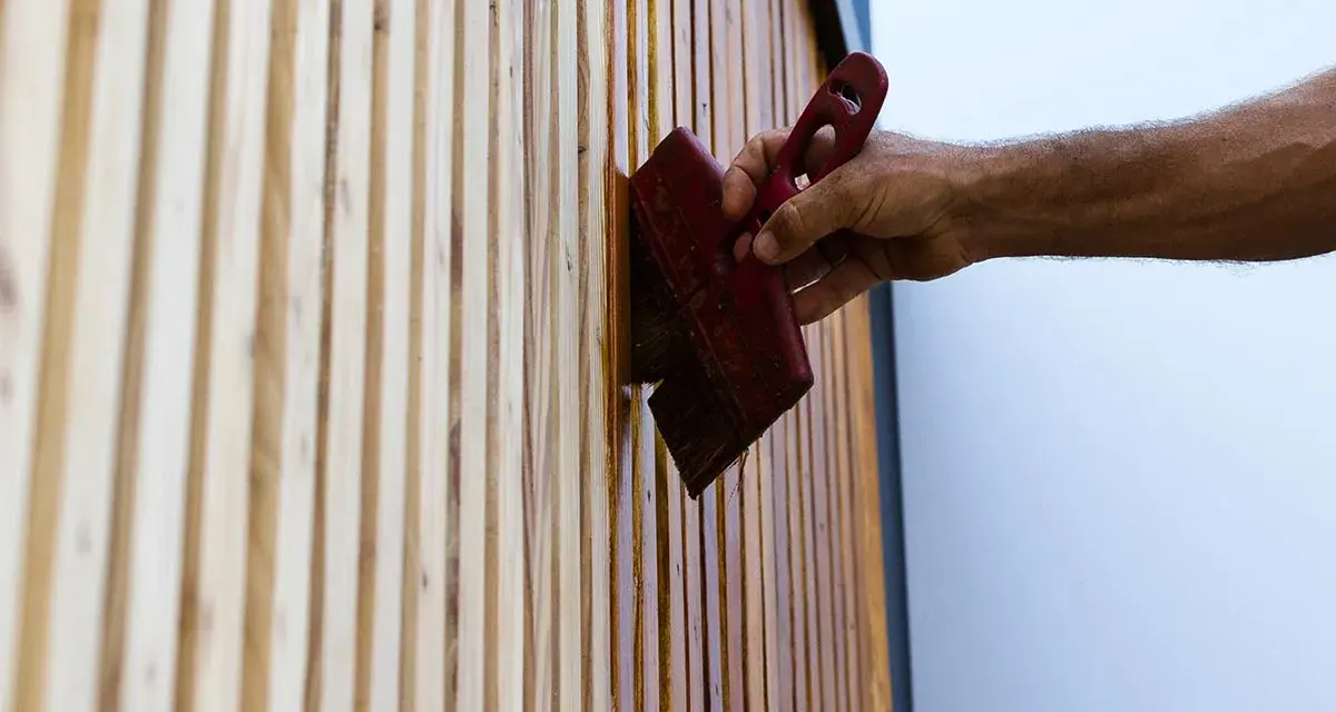 Maintenir son bois en parfait état : une main applique une huile protectrice sur des lattes de bois, comme pour fabriquer son huile de teck.