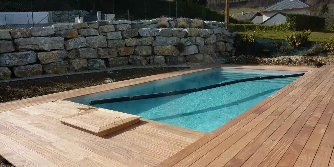 Piscine en bois avec terrasse en bois, mur de soutènement en pierre. Entretien piscine bois facile avec cette belle installation.