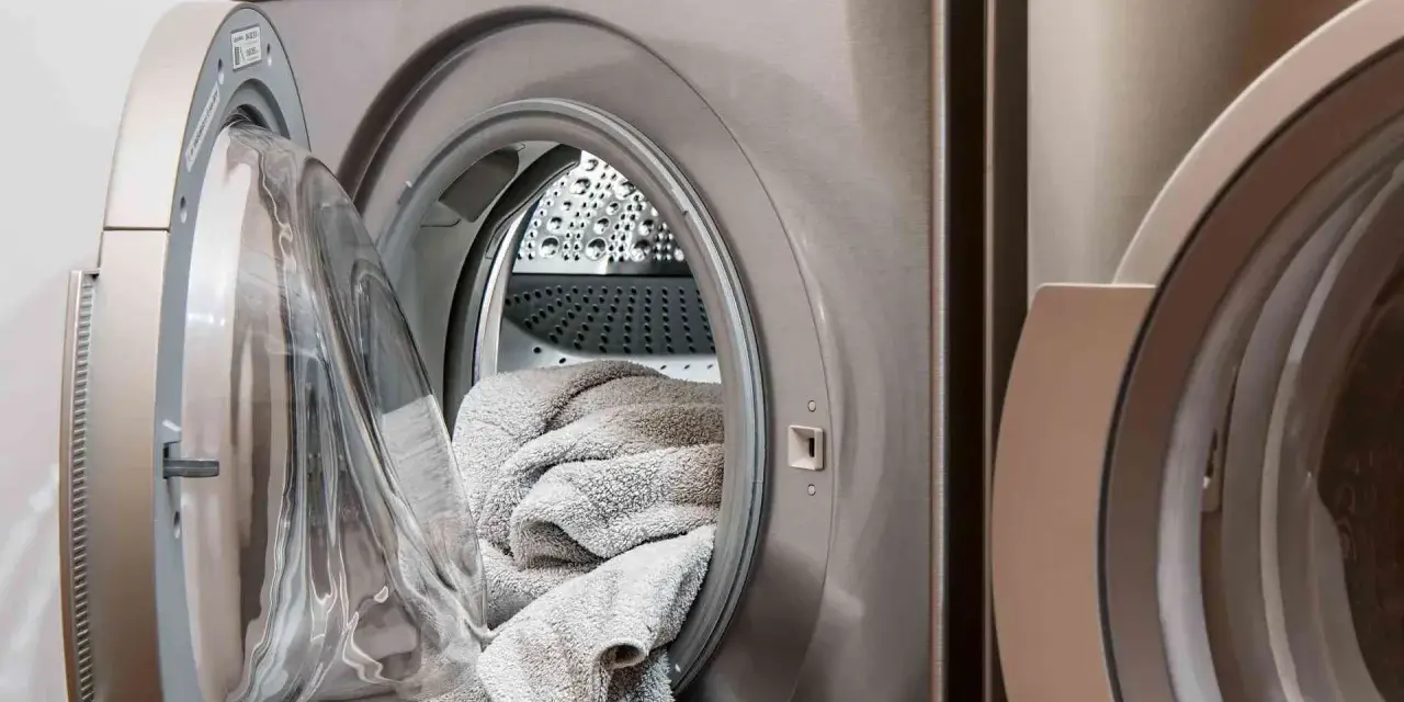 Machine à laver avec une porte ouverte, remplie de linge gris. Choisir la lessive la moins toxique pour un lavage sain.