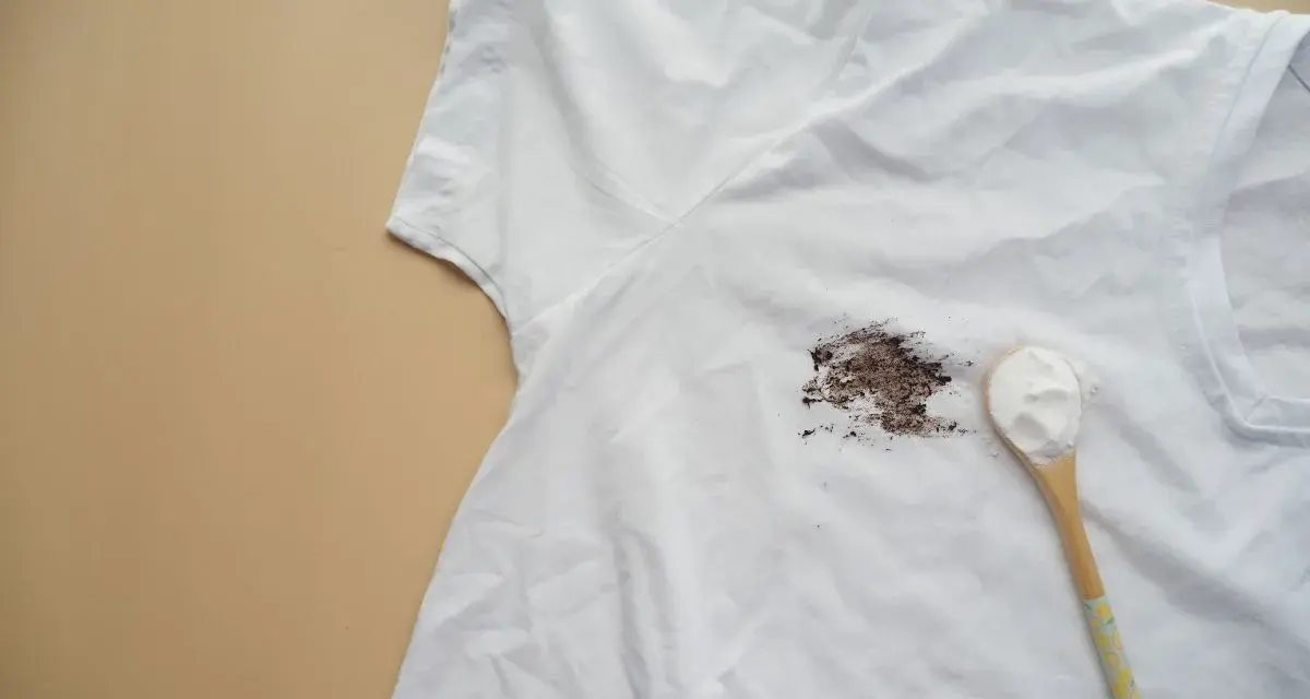 Tache sur t-shirt blanc après lavage, avec une cuillère de poudre blanche à côté.