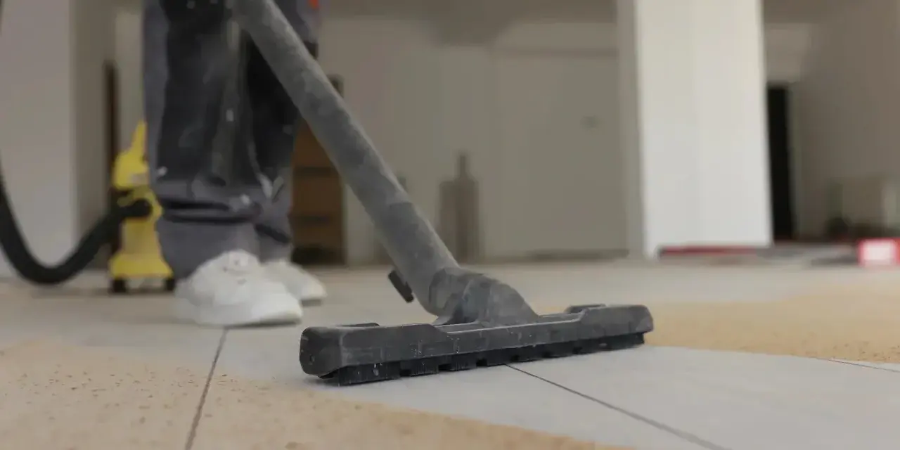 Un aspirateur en action pour enlever l'enduit sur le carrelage. La poussière est aspirée, laissant le sol propre.
