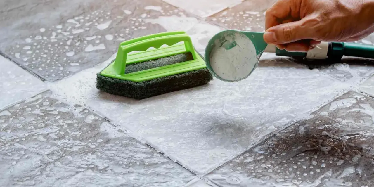Nettoyer carrelage poreux : une brosse verte et une cuillère de poudre nettoyante sur un sol mouillé et savonneux.