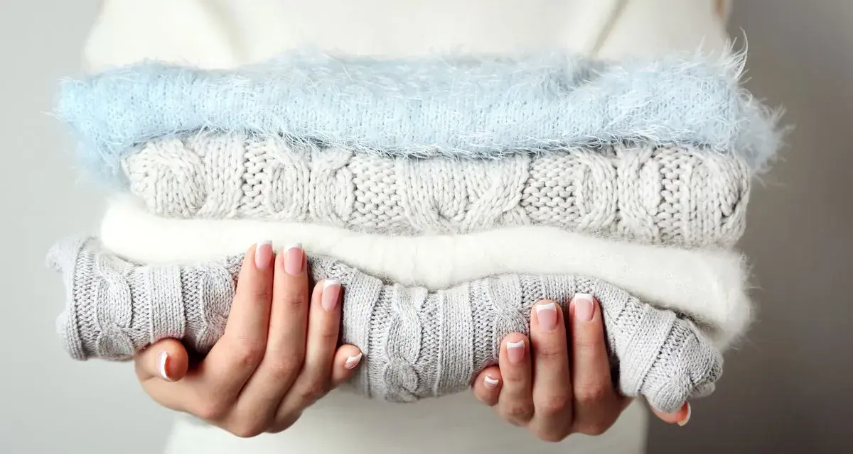 Pile de pulls en laine douce, gris et blanc, avec un pull bleu ciel. Idéal pour savoir comment detacher un pull blanc et le garder comme neuf.