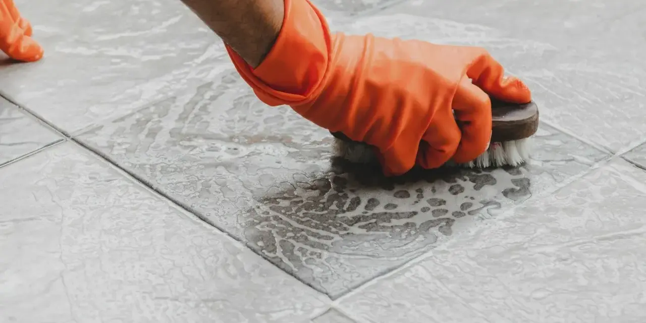 Main tenant, ganté, frotte le sol carrelé avec une brosse pour nettoyer le ciment sec.