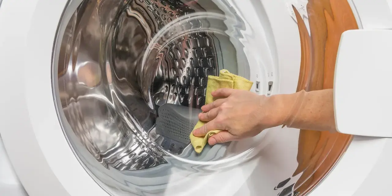 Main d'une personne utilisant un chiffon jaune pour nettoyer l'intérieur d'une machine à laver, une méthode naturelle pour nettoyer machine a laver vinaigre.