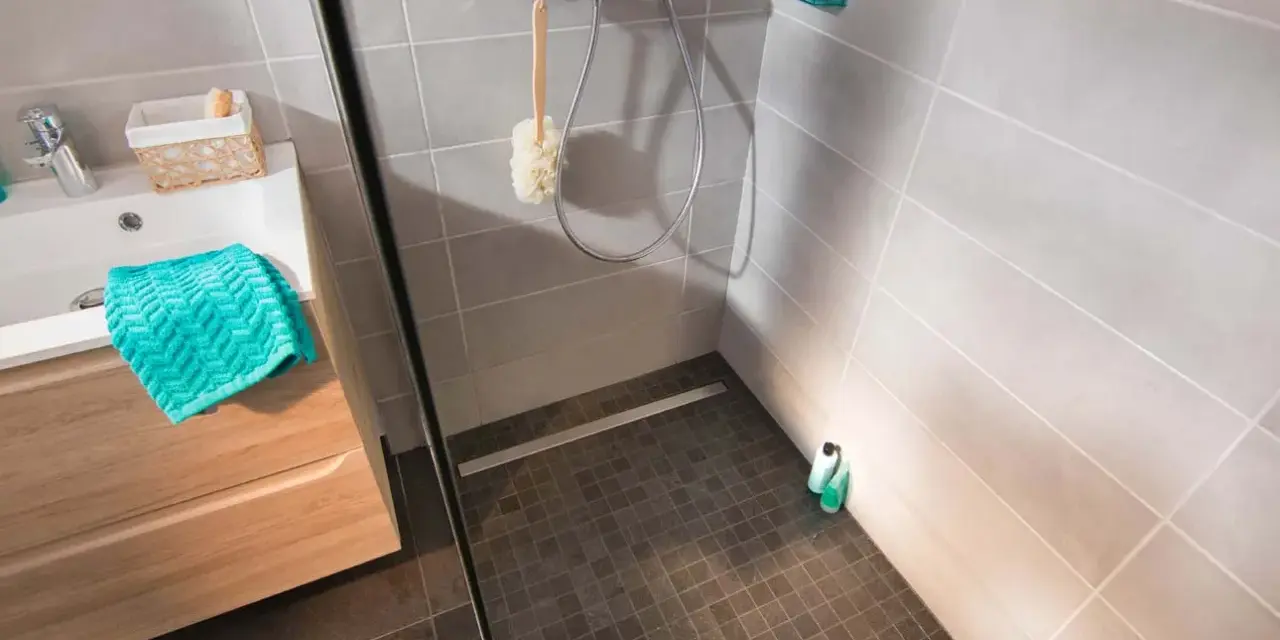 Sol de douche en galets sombres, contrastant avec le carrelage clair des murs. Une paroi vitrée sépare l'espace.