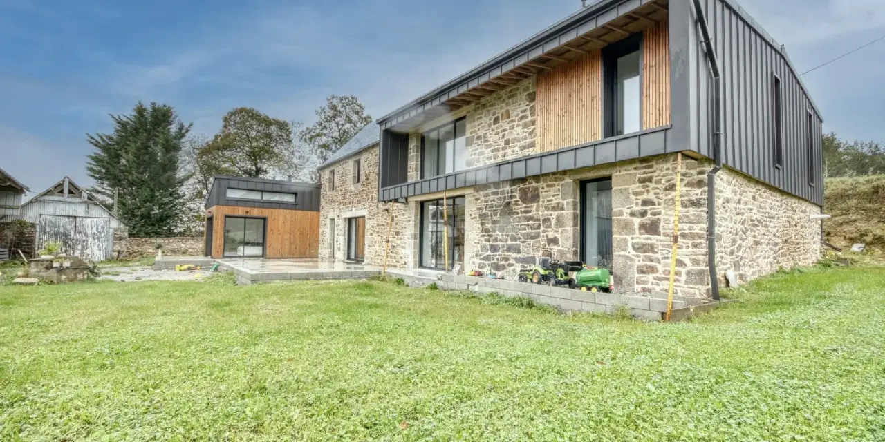 Une maison en pierre rénovée, mêlant tradition et modernité avec des touches de bois et de métal. Un jardin verdoyant entoure cette demeure.
