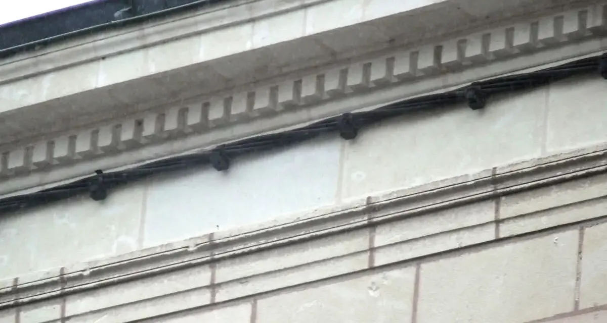 Détail d'une façade en tuffeau avec des câbles noirs fixés. L'image montre comment poncer du tuffeau pour restaurer sa surface.